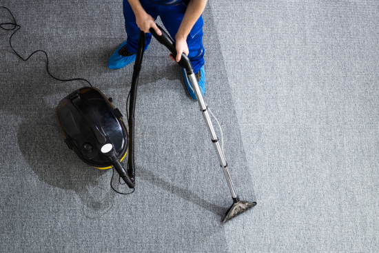 Person cleaning a gray carpet with a bagless vacuum cleaner in a living room