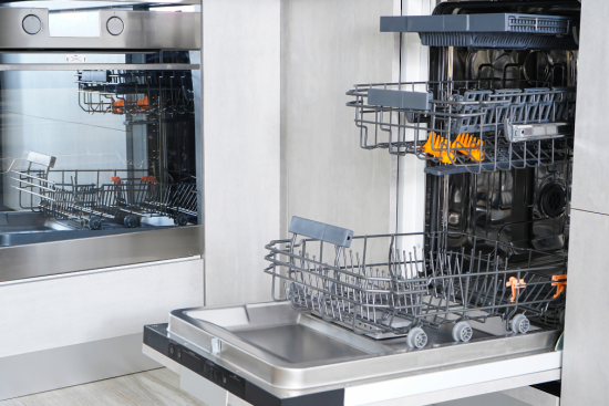 An open, empty dishwasher with stainless steel interior and racks extended, set in a modern kitchen next to a built-in oven.