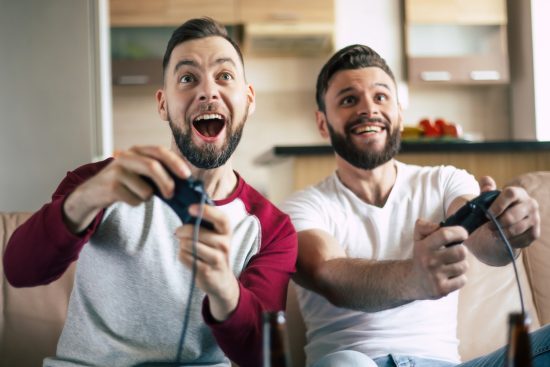 Two excited men playing video games on a console at home, enjoying a gaming session