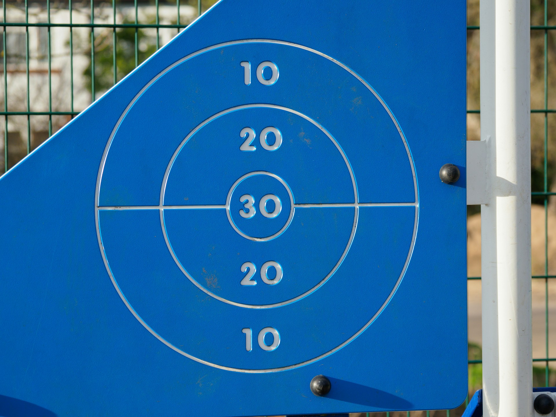 A blue plastic scoring target with concentric rings labeled 10, 20, and 30, mounted on an outdoor play structure.