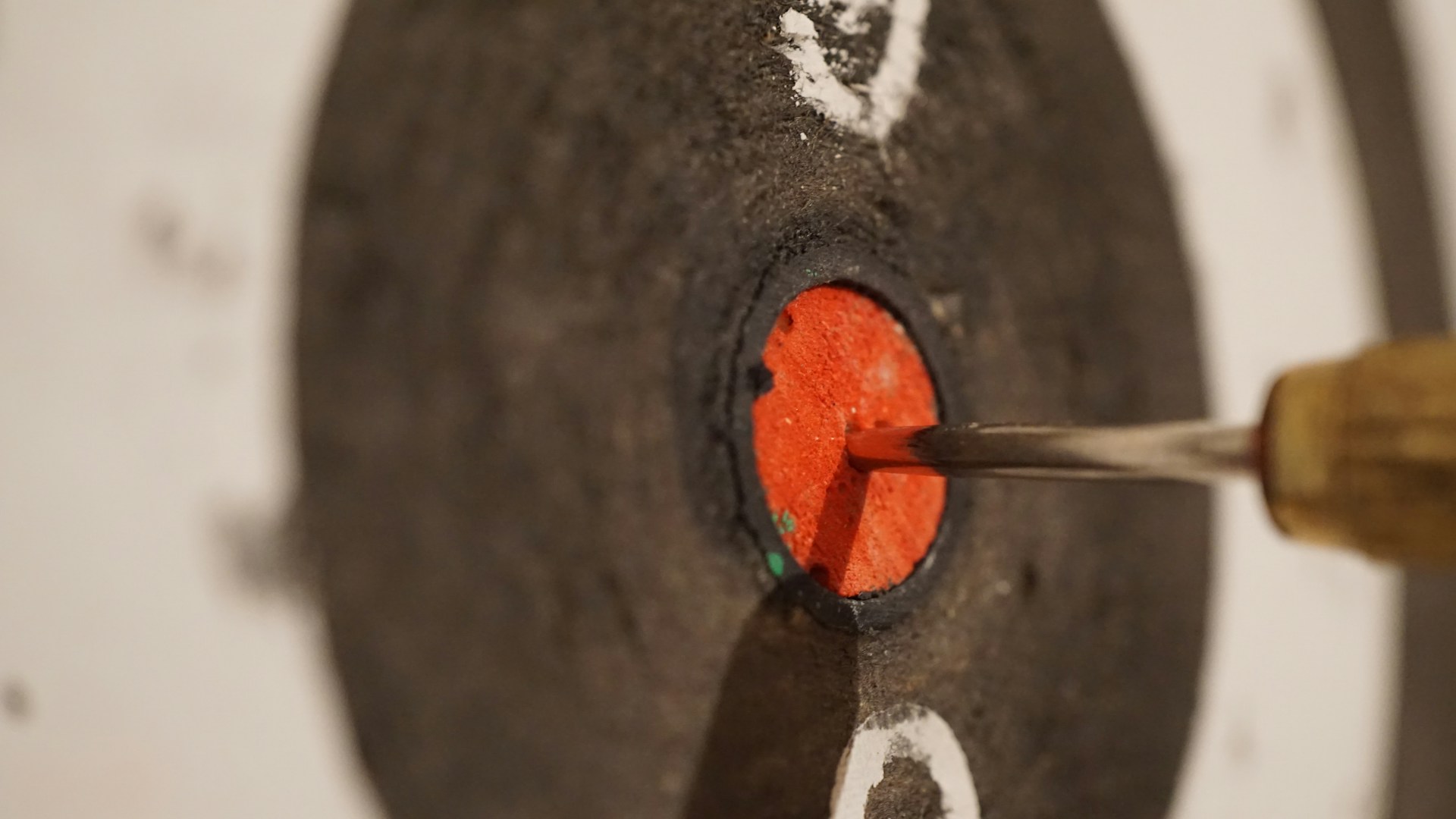 A close-up of a dart hitting the bullseye on a black and red target at an indoor range.
