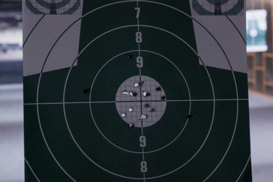 Close-up of a paper shooting target with multiple bullet holes clustered around the center at an indoor shooting range.