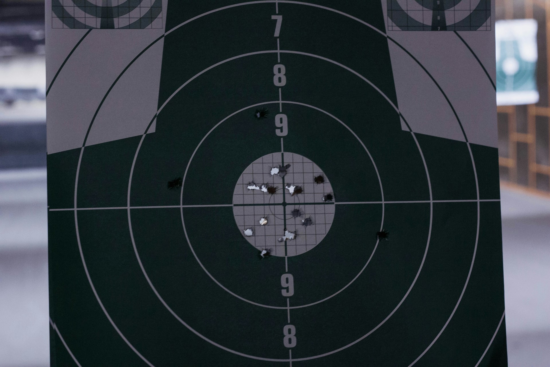 Close-up of a paper shooting target with multiple bullet holes clustered around the center at an indoor shooting range.