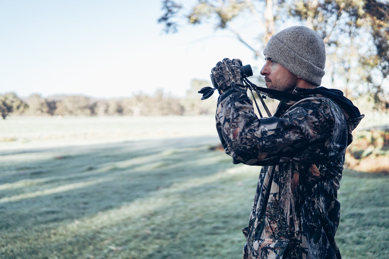 A man in camo gear uses binoculars while scouting a hunting area on a cold morning.