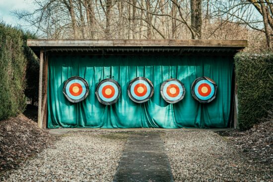 Five colorful archery targets lined up under a wooden shelter at an outdoor practice range.