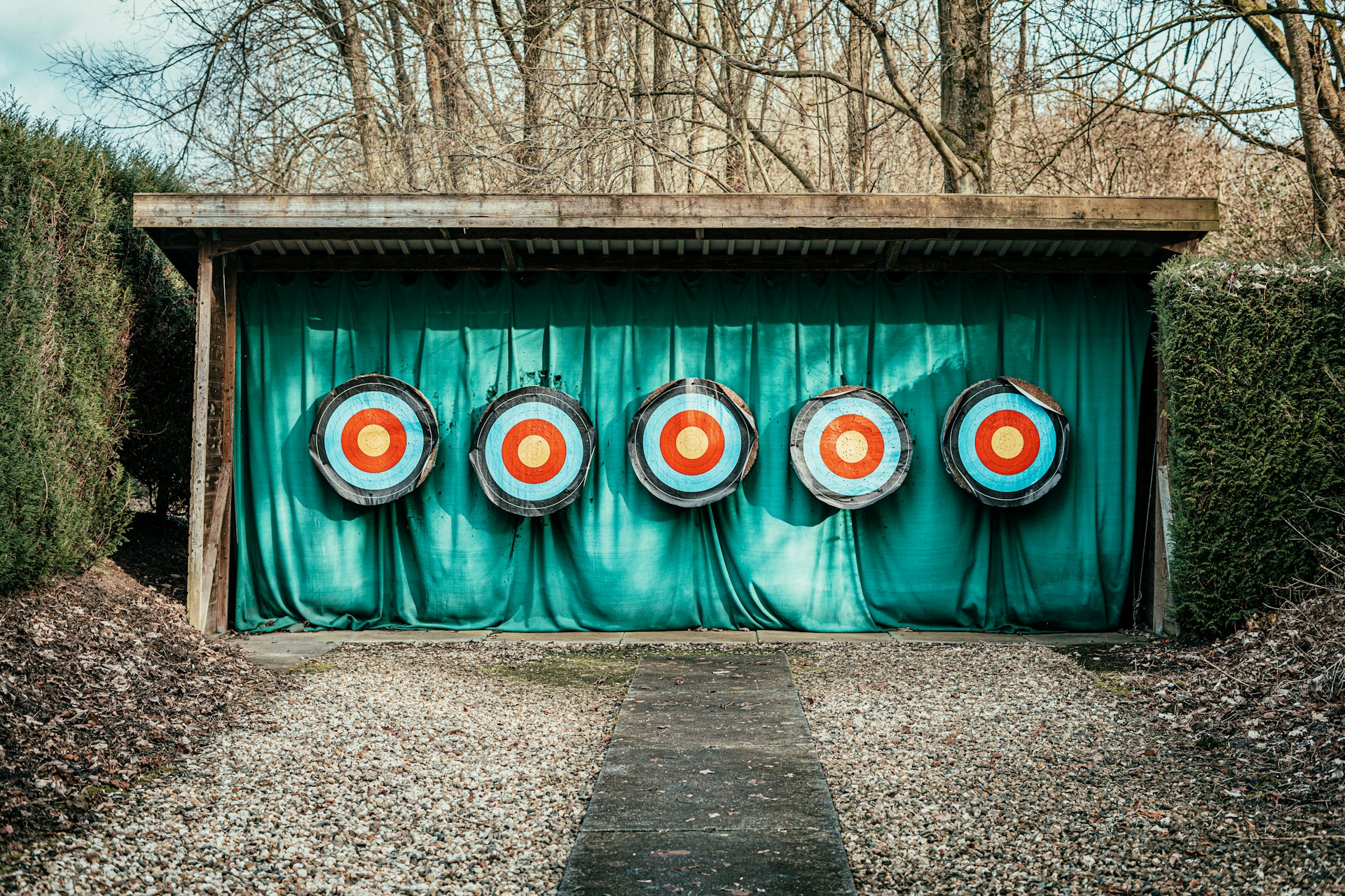 Five colorful archery targets lined up under a wooden shelter at an outdoor practice range.