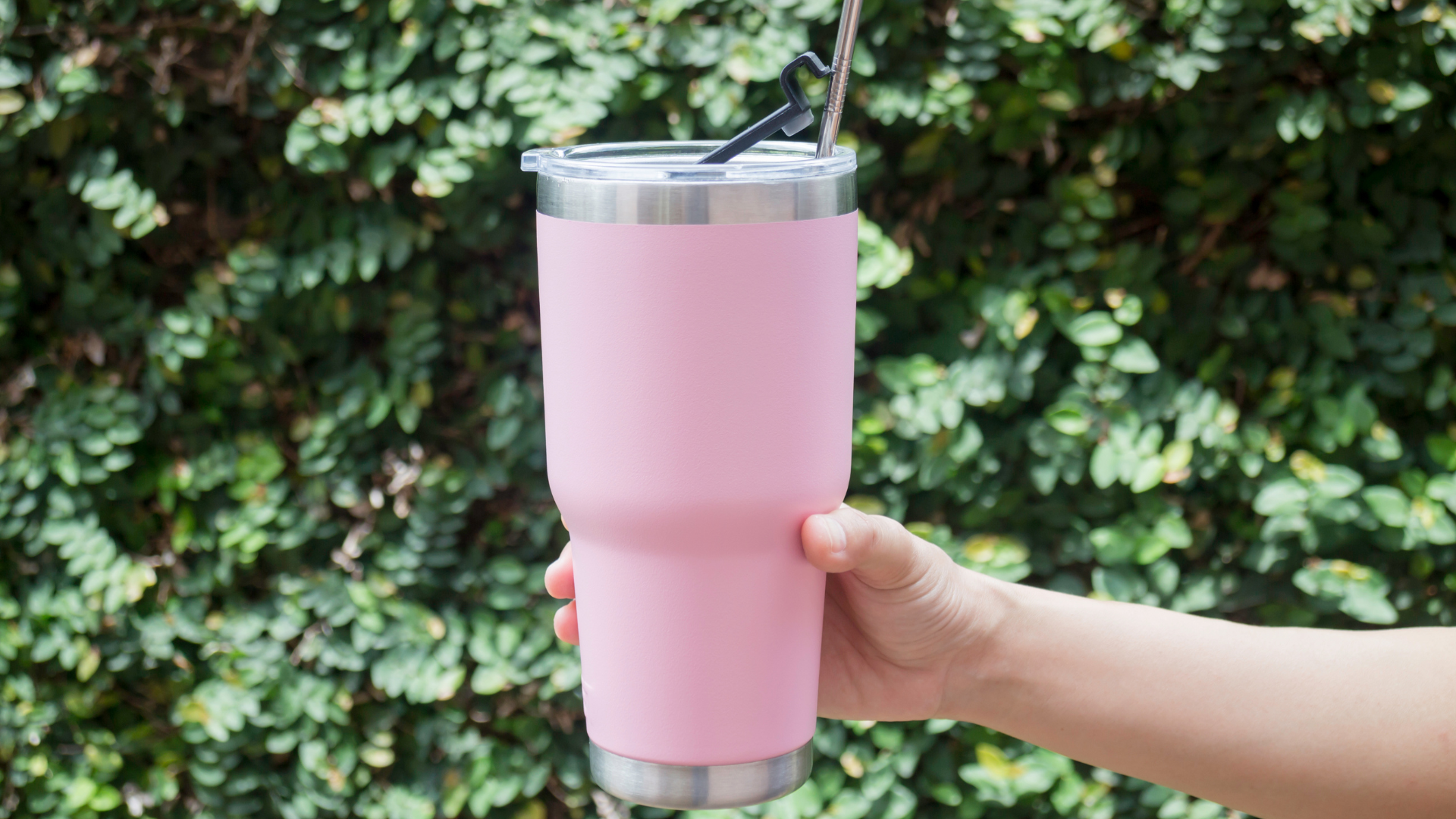 Person holding a vacuum insulated tumbler on a nature-rich background.