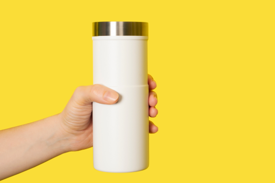 A hand holding a white tumbler with a silver lid, set against a bright yellow background.