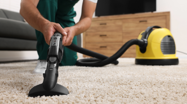 A person wearing green using a vacuum cleaner.