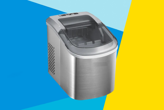 A stainless steel countertop ice maker with a transparent lid, set against a vibrant background of blue and yellow geometric shapes.