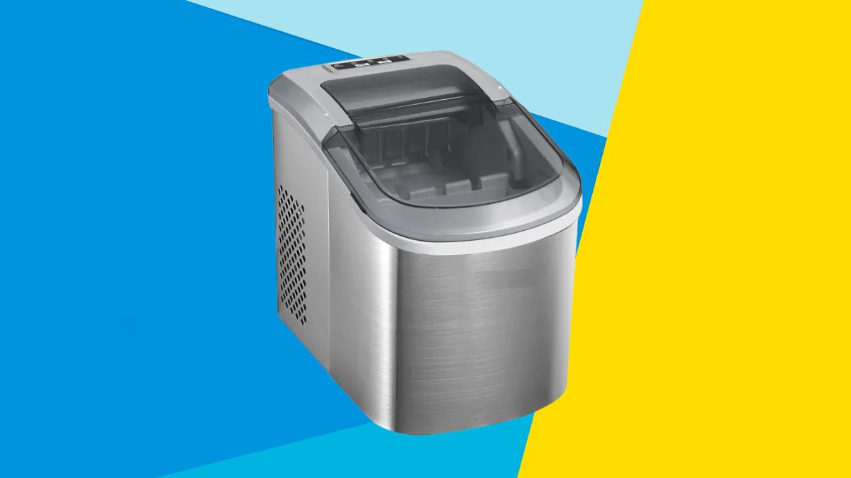 A stainless steel countertop ice maker with a transparent lid, set against a vibrant background of blue and yellow geometric shapes.