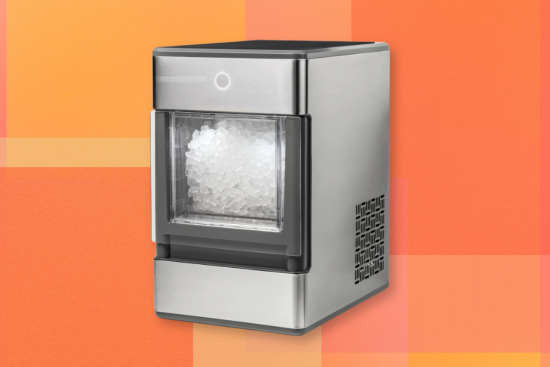 A stainless steel countertop ice maker filled with ice, set against a vibrant orange background with subtle geometric patterns.