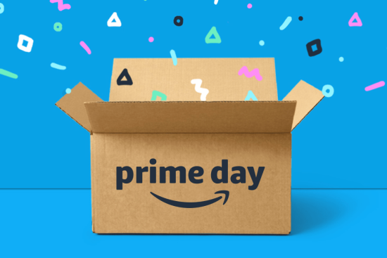 An open cardboard box with the 'Amazon Prime Day' logo displayed on the front. Colorful confetti-like shapes are flying out of the box against a bright blue background, symbolizing the excitement and celebration of Amazon's Prime Day shopping event.