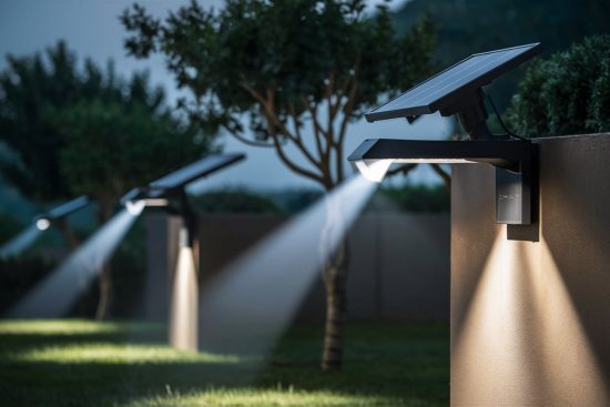 Row of solar-powered LED lights mounted on a garden wall, casting bright beams of light onto the grass at night.