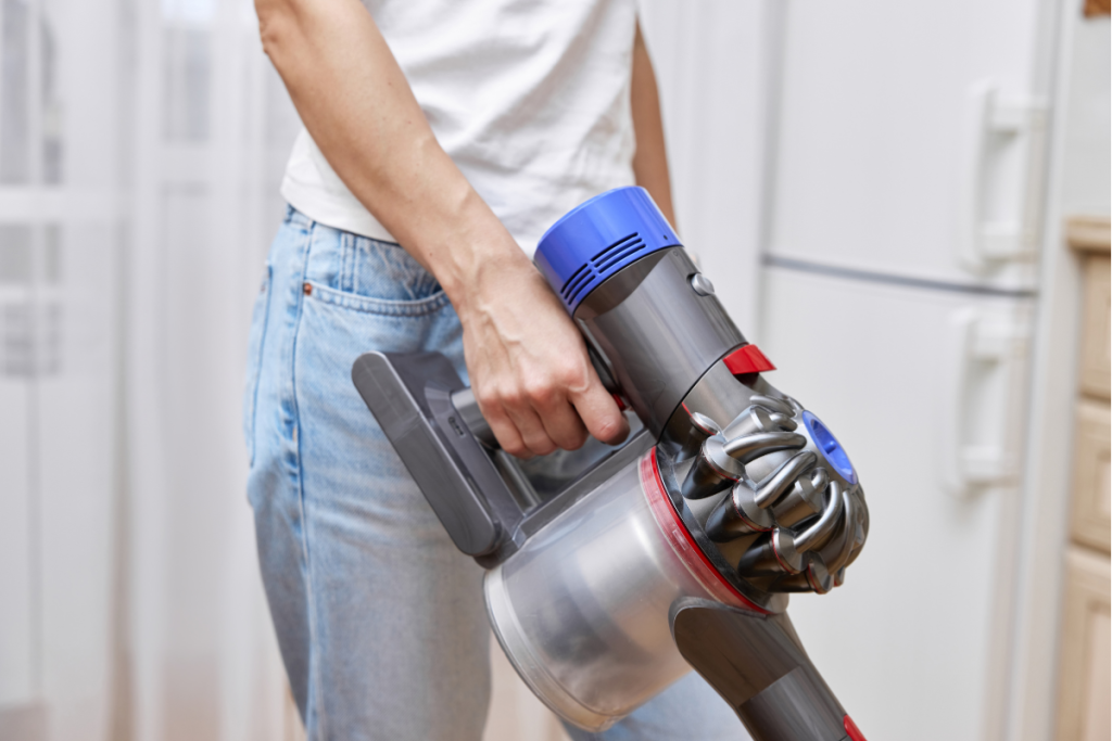 A person holding a cordless handheld vacuum cleaner in a kitchen.