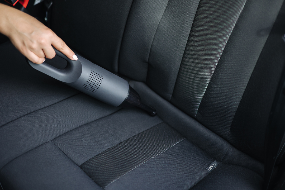 A person using a handheld vacuum cleaner to clean the back seat of a car.