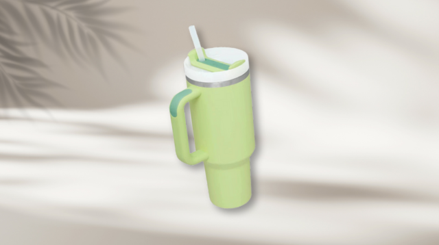 A green tumbler cup with a handle and straw, set against a blurred, soft background with light shadows.