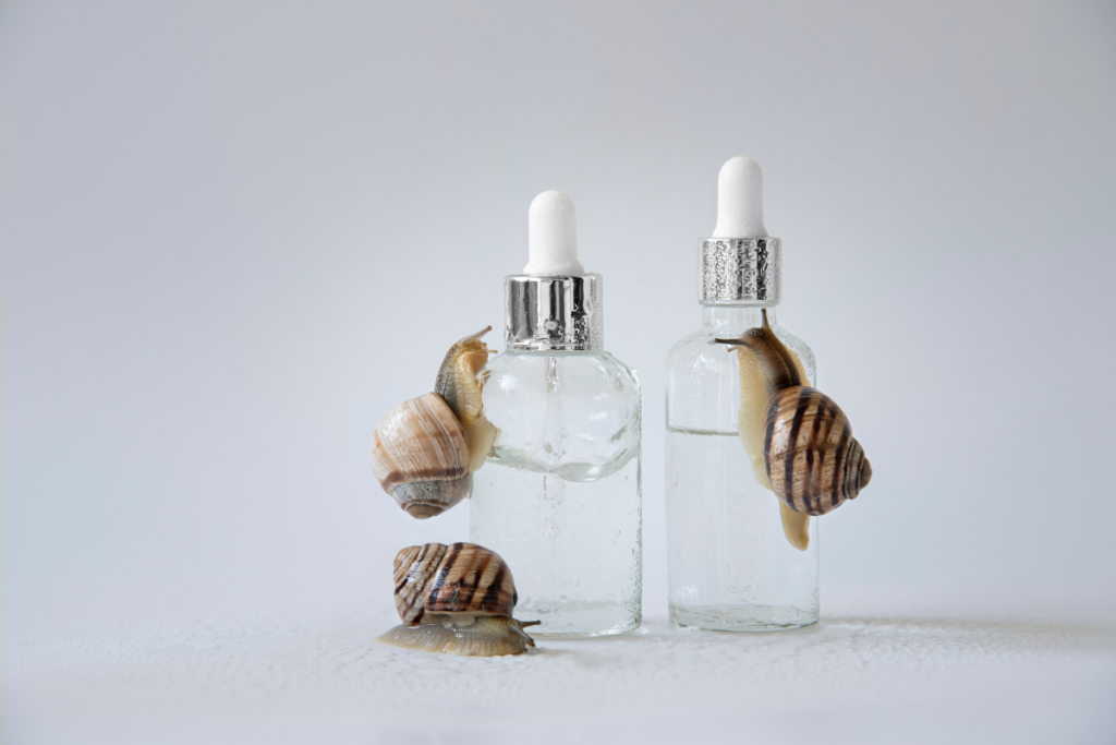 Two dropper bottles filled with clear liquid, with snails crawling on and around them on a light background.