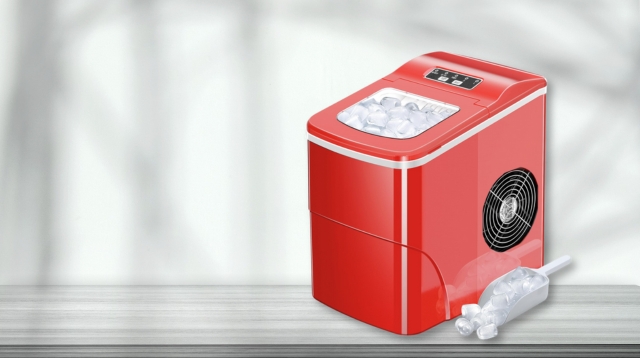 A red countertop ice maker with visible ice in the top compartment, sitting on a wooden surface, with an ice scoop and a small pile of ice cubes beside it.