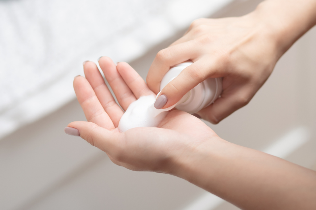 A person dispensing foam cleanser into their palm in a bathroom setting.