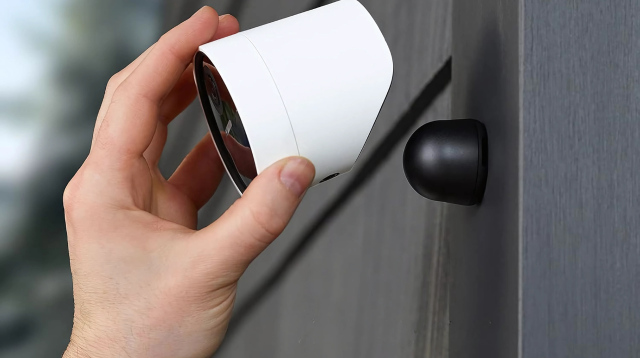 A person installing or adjusting a white outdoor security camera onto a magnetic wall mount