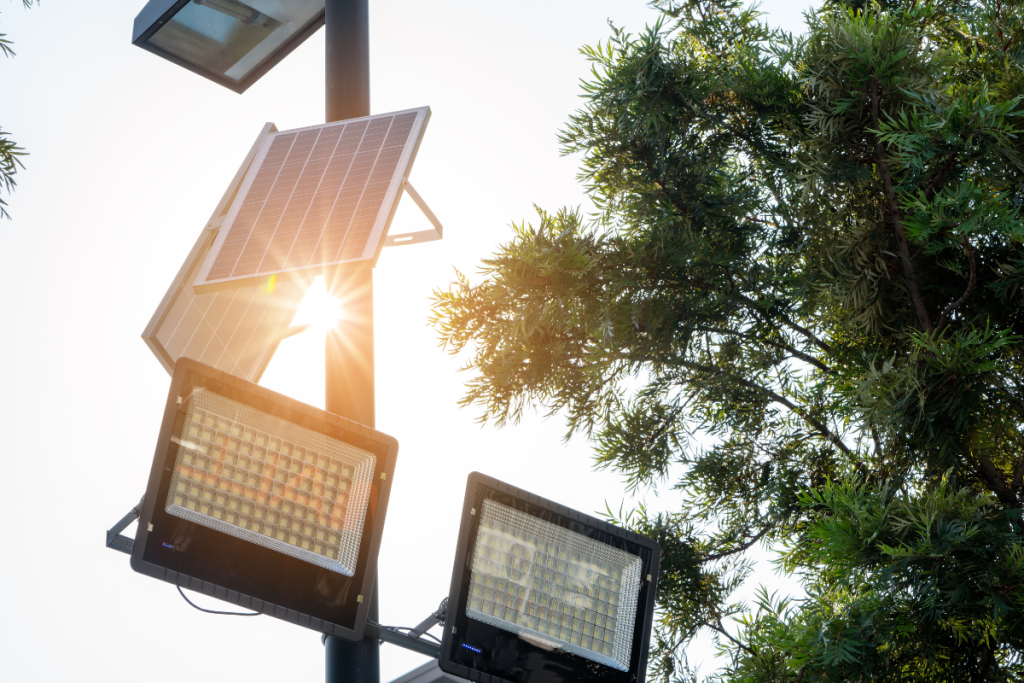 Solar-powered LED streetlights mounted on a pole, with solar panels capturing sunlight, surrounded by trees.