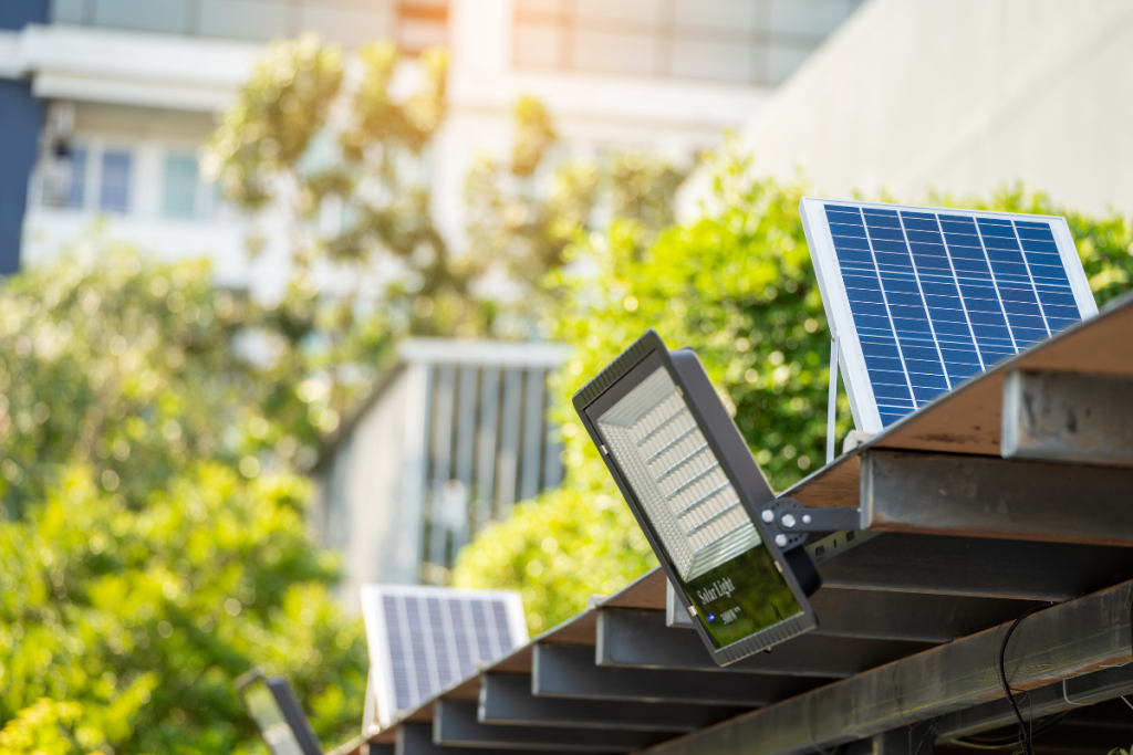 Outdoor solar-powered LED floodlight mounted on a metal frame, connected to a solar panel under daylight.