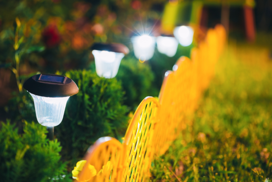 Solar-powered garden lights illuminating a pathway along a yellow decorative fence at night.