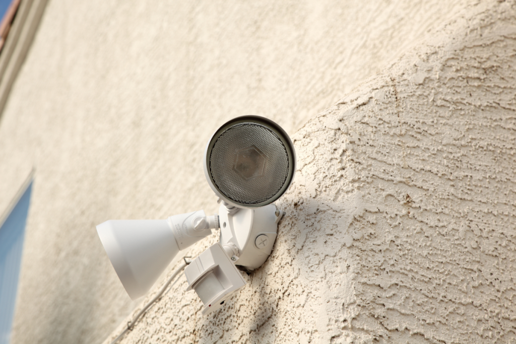 Outdoor motion-activated security light with dual floodlights mounted on a stucco wall.