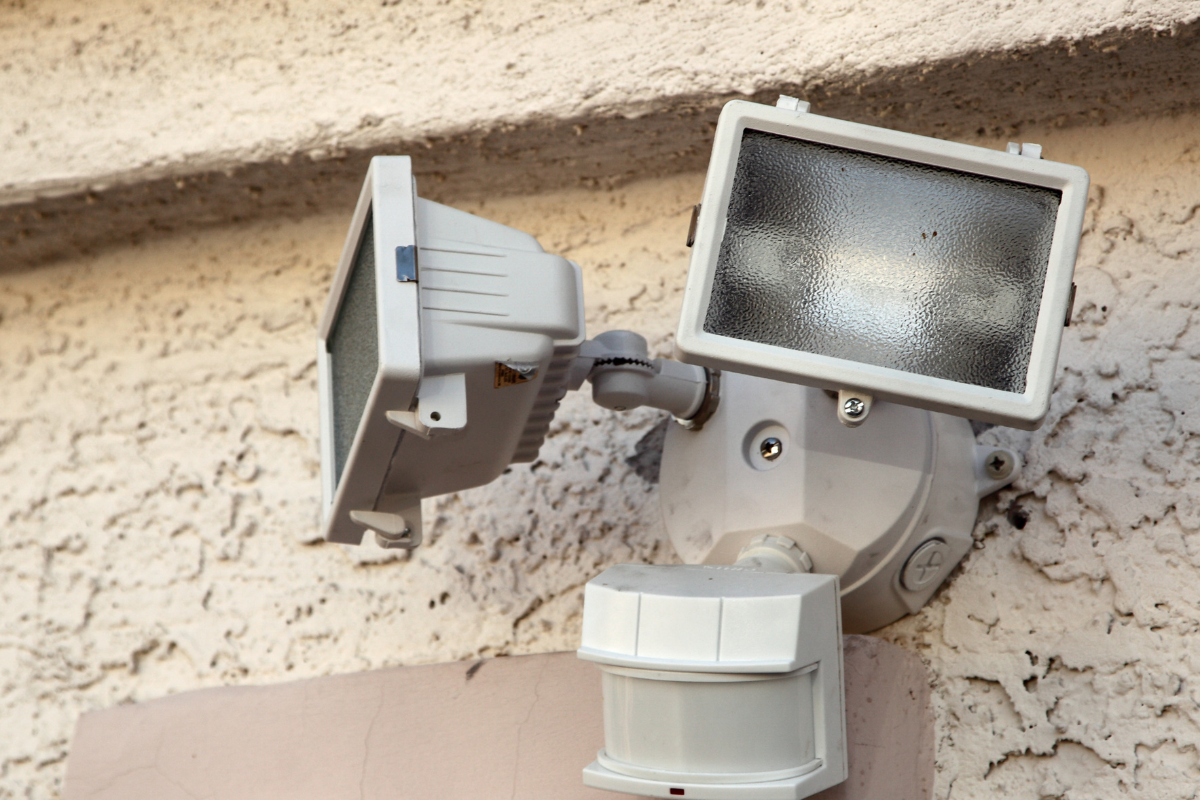 Dual-head outdoor floodlight with motion sensor mounted on a textured wall.