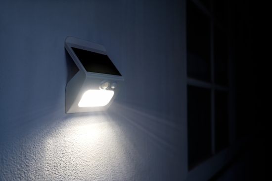 Wall-mounted solar motion sensor light illuminating a dark exterior surface at night.