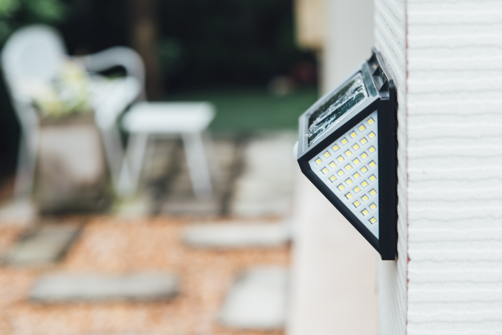 Side view of a wall-mounted solar LED light with a blurred outdoor patio area in the background.