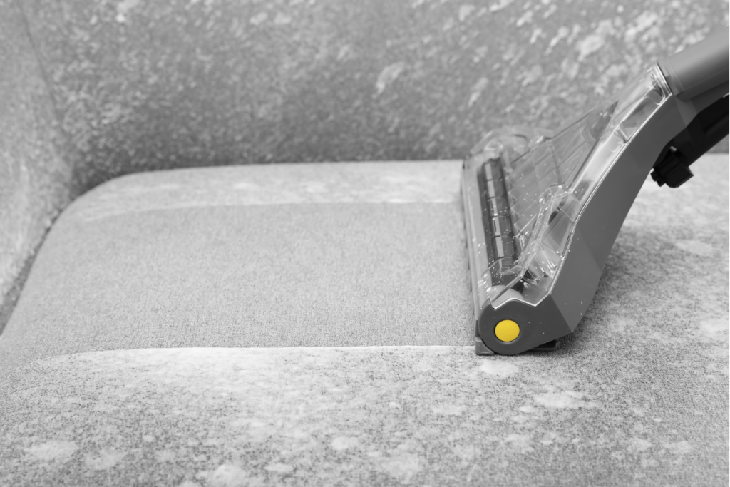 A vacuum cleaner being used to deep clean and remove stains from a fabric seat cushion.