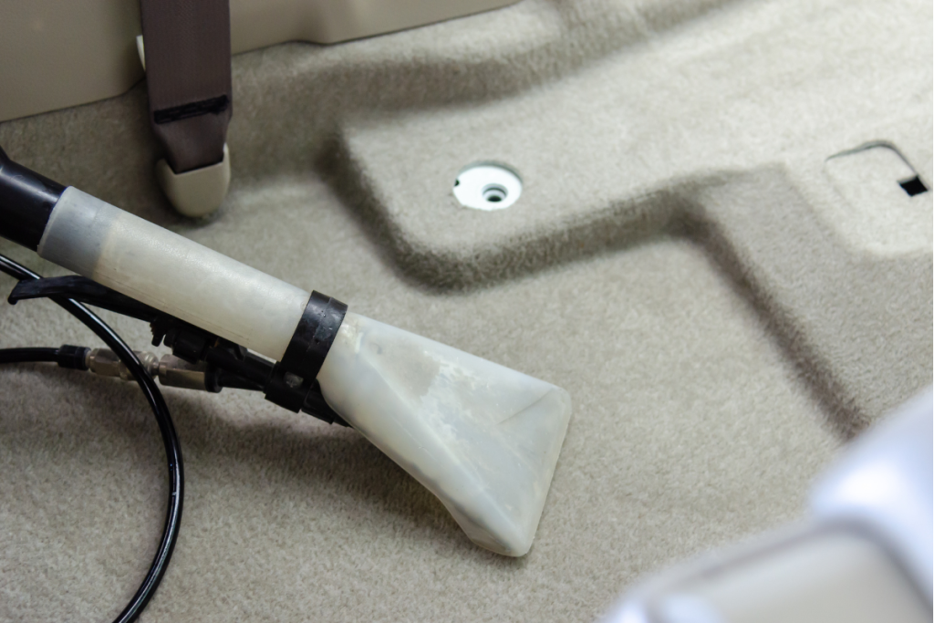 A vacuum cleaner attachment being used to clean the carpet floor of a car.