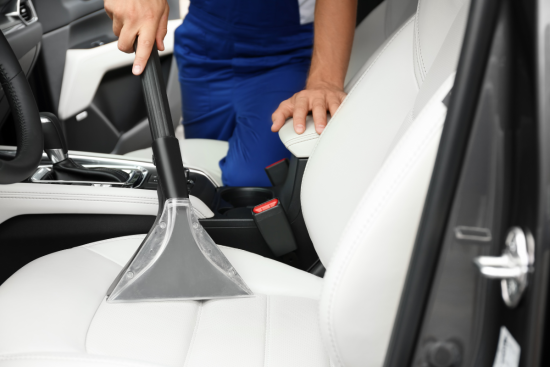 A person using a vacuum cleaner to clean the white leather seat of a car.