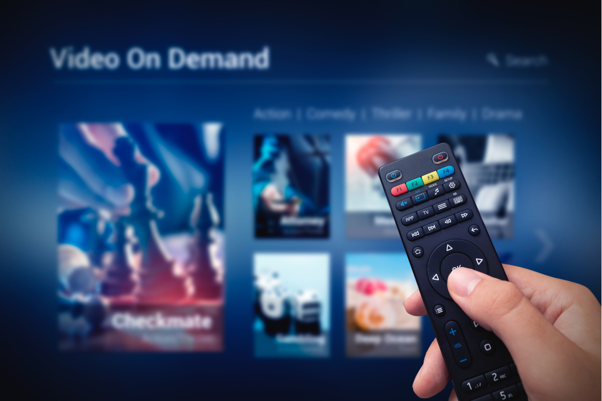 A person holding a remote control while browsing video on demand content on a TV screen.