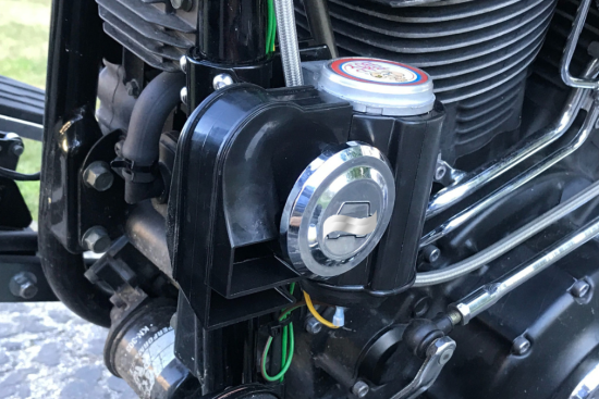 This image showcases a motorcycle engine with a detailed view of its components, highlighting a black aftermarket horn unit and surrounding mechanical parts.