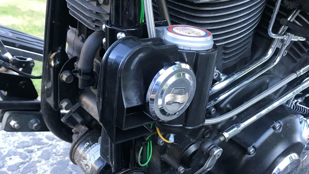 This image showcases a motorcycle engine with a detailed view of its components, highlighting a black aftermarket horn unit and surrounding mechanical parts.