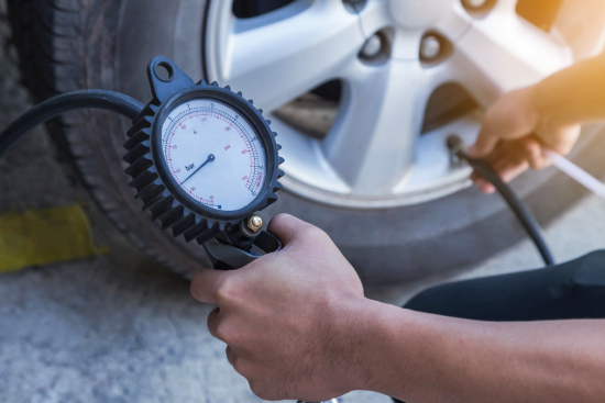 This image features a person checking the tire pressure of a vehicle using a tire pressure gauge.