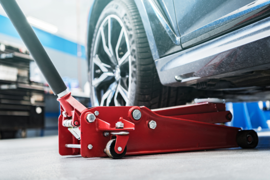 This image shows a red hydraulic floor jack lifting a car, commonly used in automotive repair and maintenance.