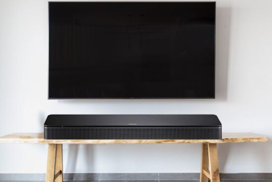 A Bose TV Speaker is placed on a wooden table beneath a mounted flat-screen TV, showing its sleek and modern design, perfect for enhancing TV audio.