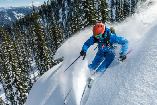 An adrenaline-filled moment of a skier in vibrant blue gear gliding through fresh powder snow on a mountain slope, surrounded by towering pine trees and a scenic winter landscape.