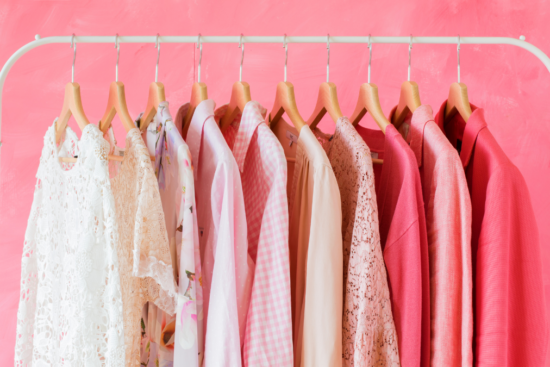 A clothing rack with neatly arranged pink and white garments, including lace, floral, and solid patterns, set against a vibrant pink background