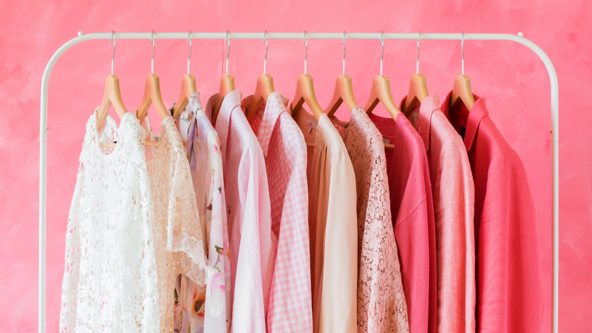 A clothing rack with neatly arranged pink and white garments, including lace, floral, and solid patterns, set against a vibrant pink background