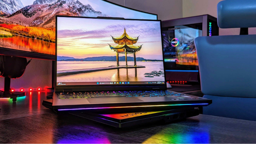A Lenovo Legion Pro 7i Gen 9 gaming laptop on a desk, illuminated with vibrant RGB lighting and a scenic wallpaper on the screen.