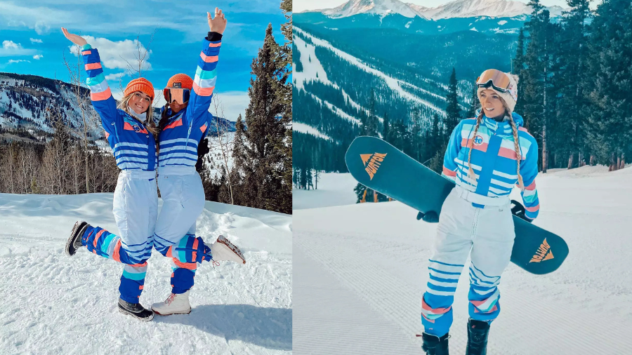 Two women in colorful blue and white ski outfits enjoying a snowy mountain setting; one is holding a snowboard, and the other is joyfully posing.