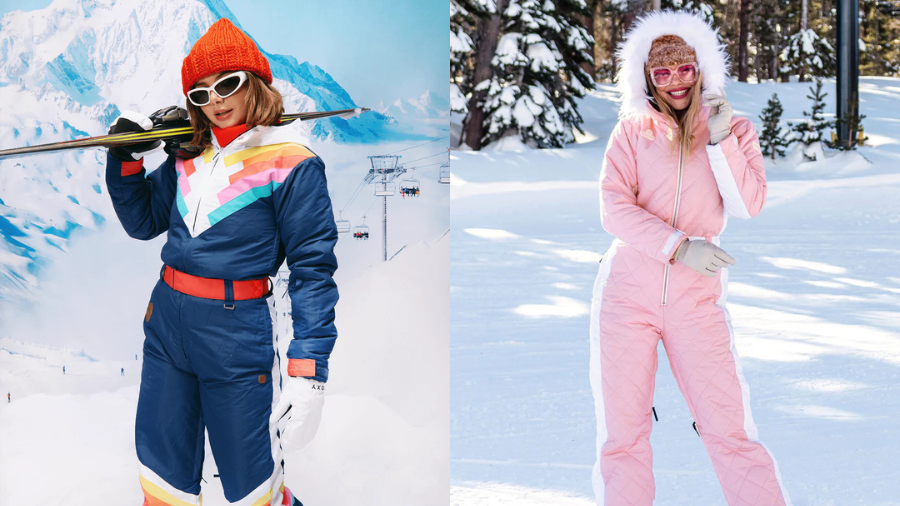 Two women in colorful ski outfits: the left wearing a retro-style navy and rainbow jumpsuit with orange accessories, holding skis, and the right in a pink fur-lined suit smiling on a snowy slope.