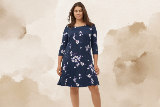 A woman wearing a navy blue dress with three-quarter sleeves and a floral pattern, standing against a beige watercolor background.