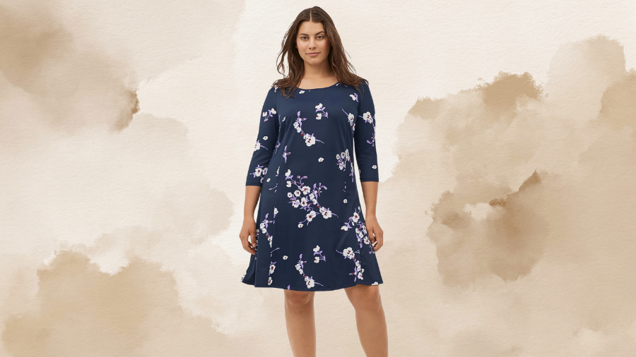 A woman wearing a navy blue dress with three-quarter sleeves and a floral pattern, standing against a beige watercolor background.