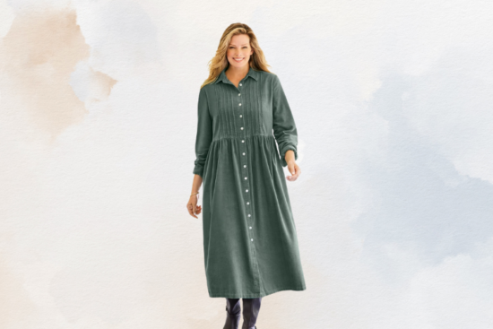 A woman wearing a long green button-down dress with long sleeves, standing against a soft pastel background.